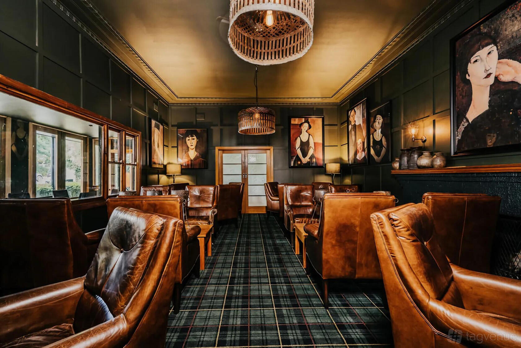 A hotel lounge with brown leather armchairs, tartan carpet, and portrait artwork at The Amalfi.