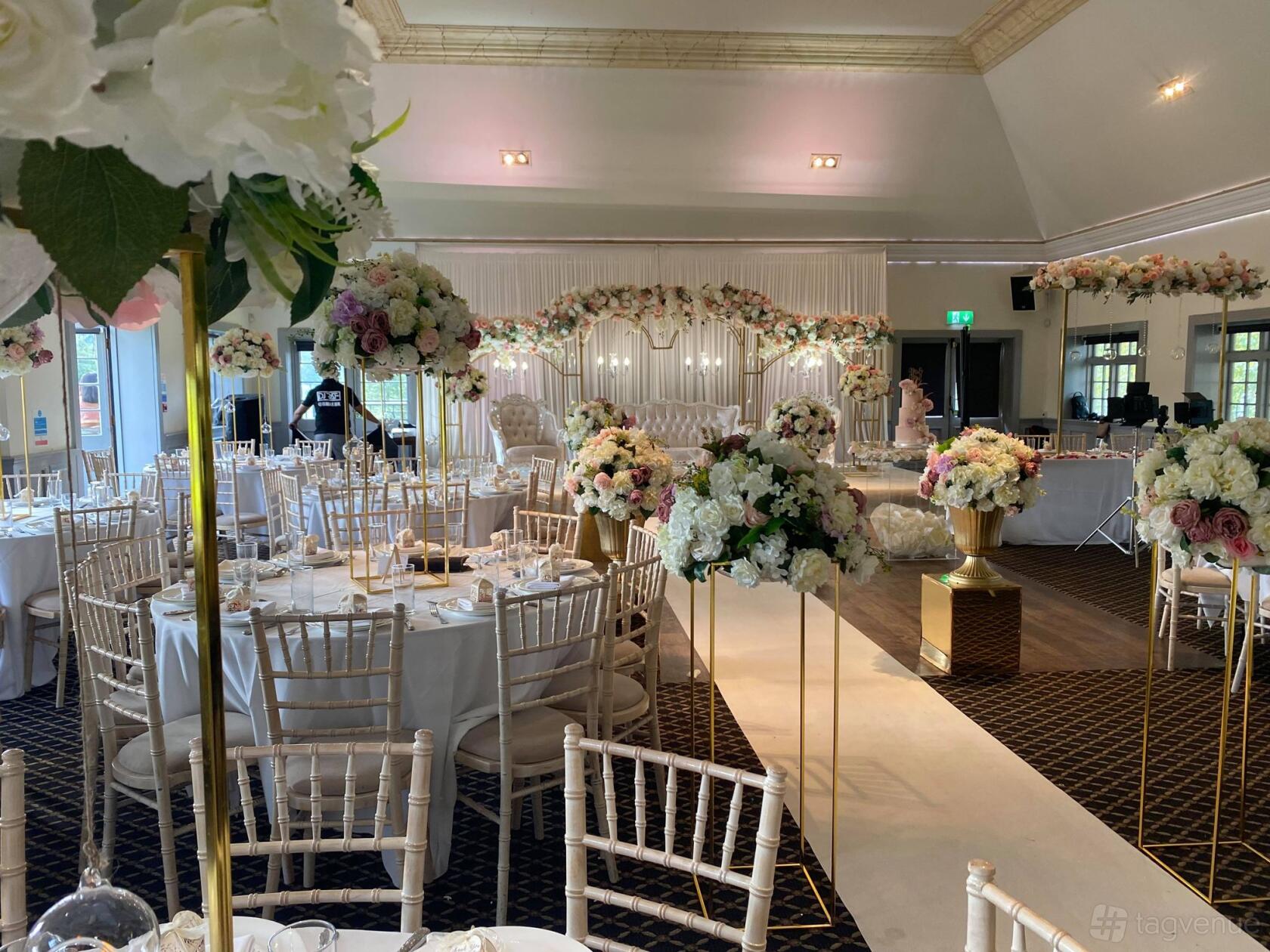 An event venue with round tables, white Chiavari chairs, and floral centerpieces at Woolston Manor Golf Club.