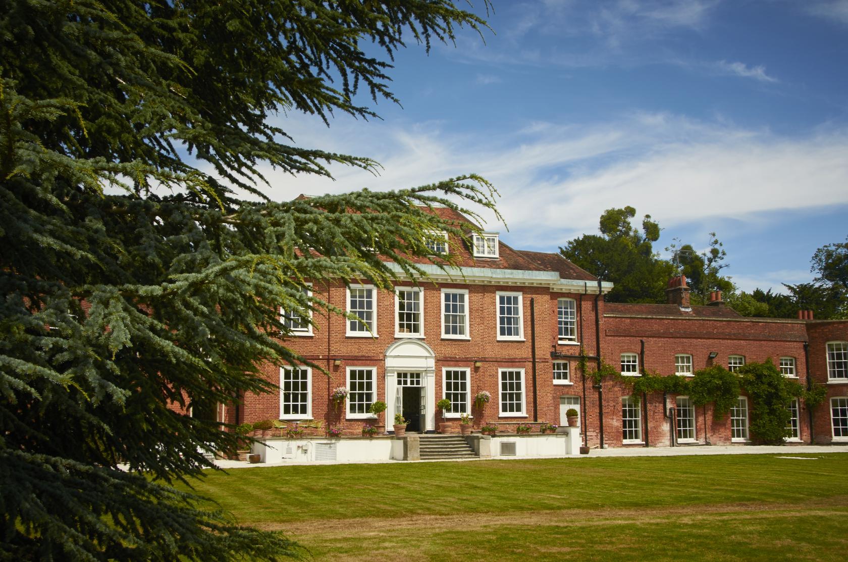 A hotel with a red brick Georgian facade, white columns, and manicured lawn at Stoke Place.