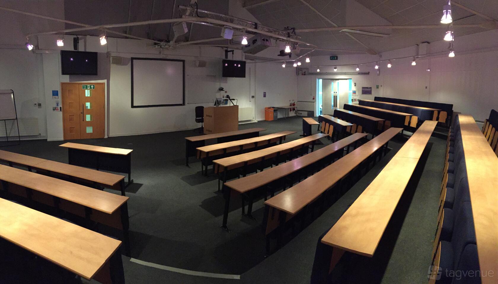 An auditorium with tiered seating, built-in projector screens, and a lectern at ARU Venue Hire - Chelmsford.