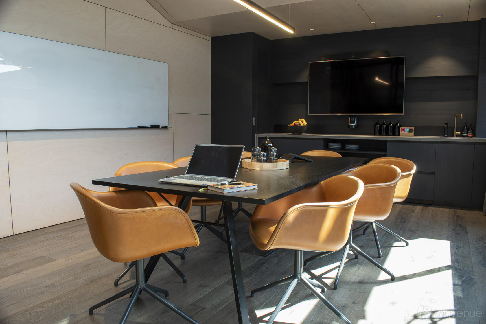 A meeting room with tan leather chairs, a large table, a wall-mounted TV, and a whiteboard at SleevesUp.