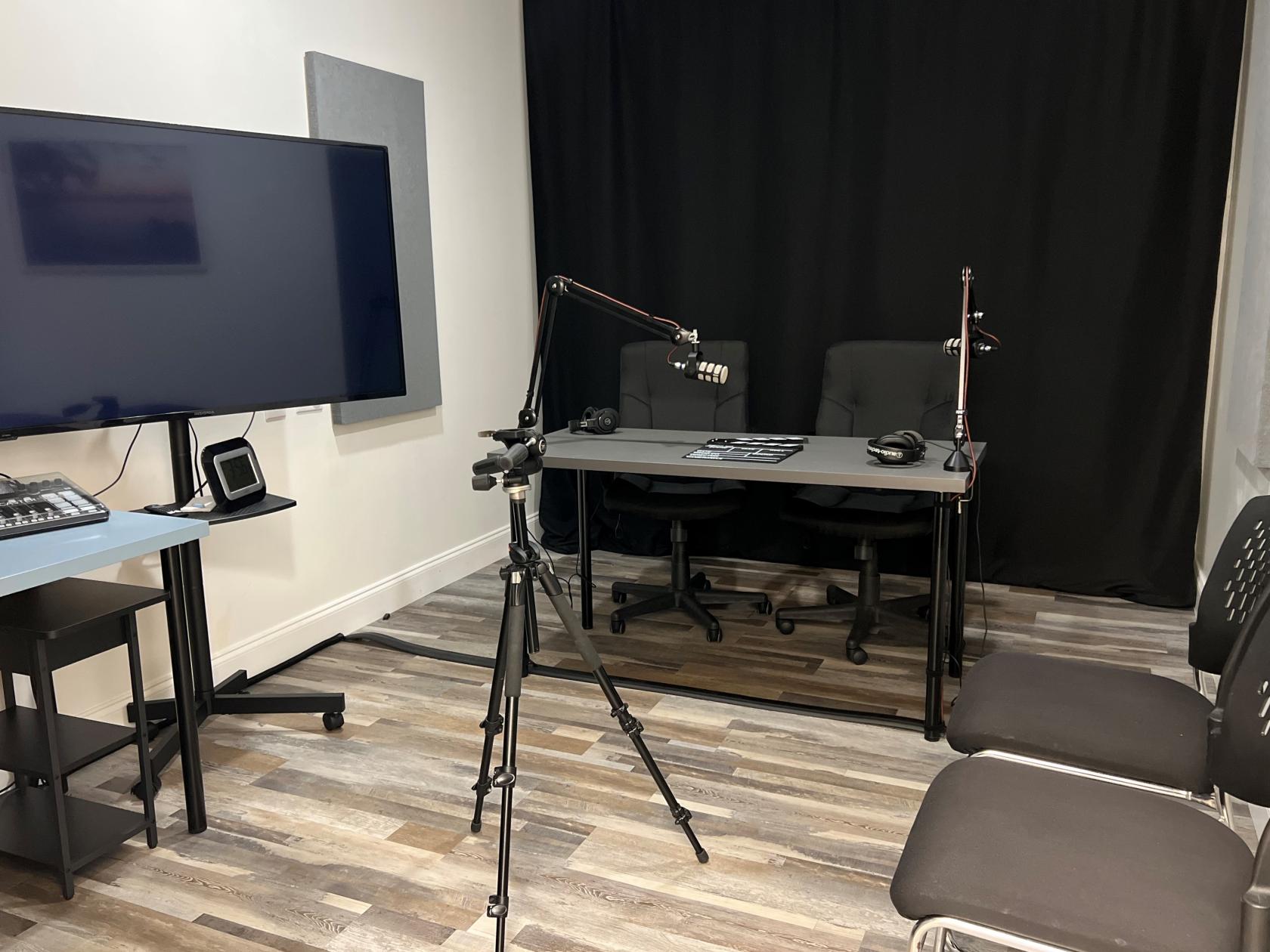A podcast studio with microphones on adjustable arms, a large monitor, tripod, and mixing console at TopNotch Content Studios.