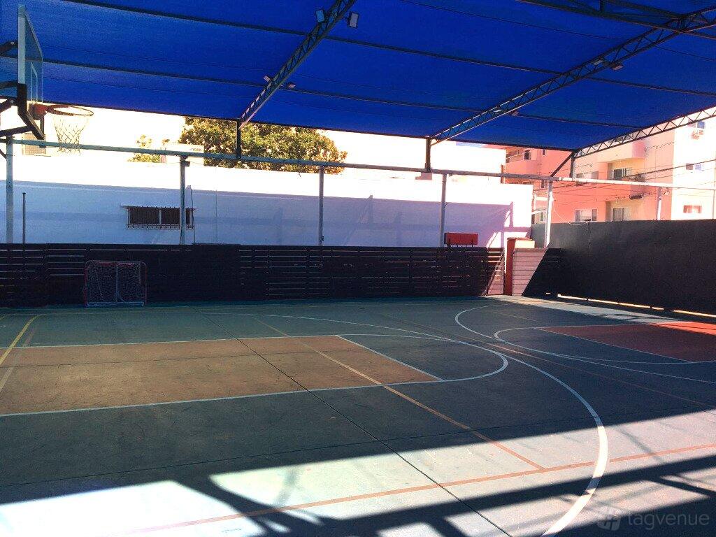 A basketball court with painted lines, a covered roof, and a visible basketball hoop at International Children's Academy.