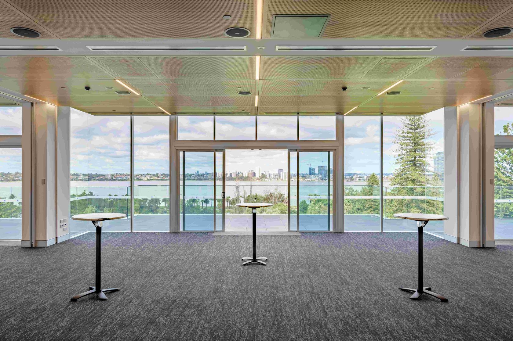 A function room with floor-to-ceiling windows, cocktail tables, and skyline views at The Anzac Club WA.
