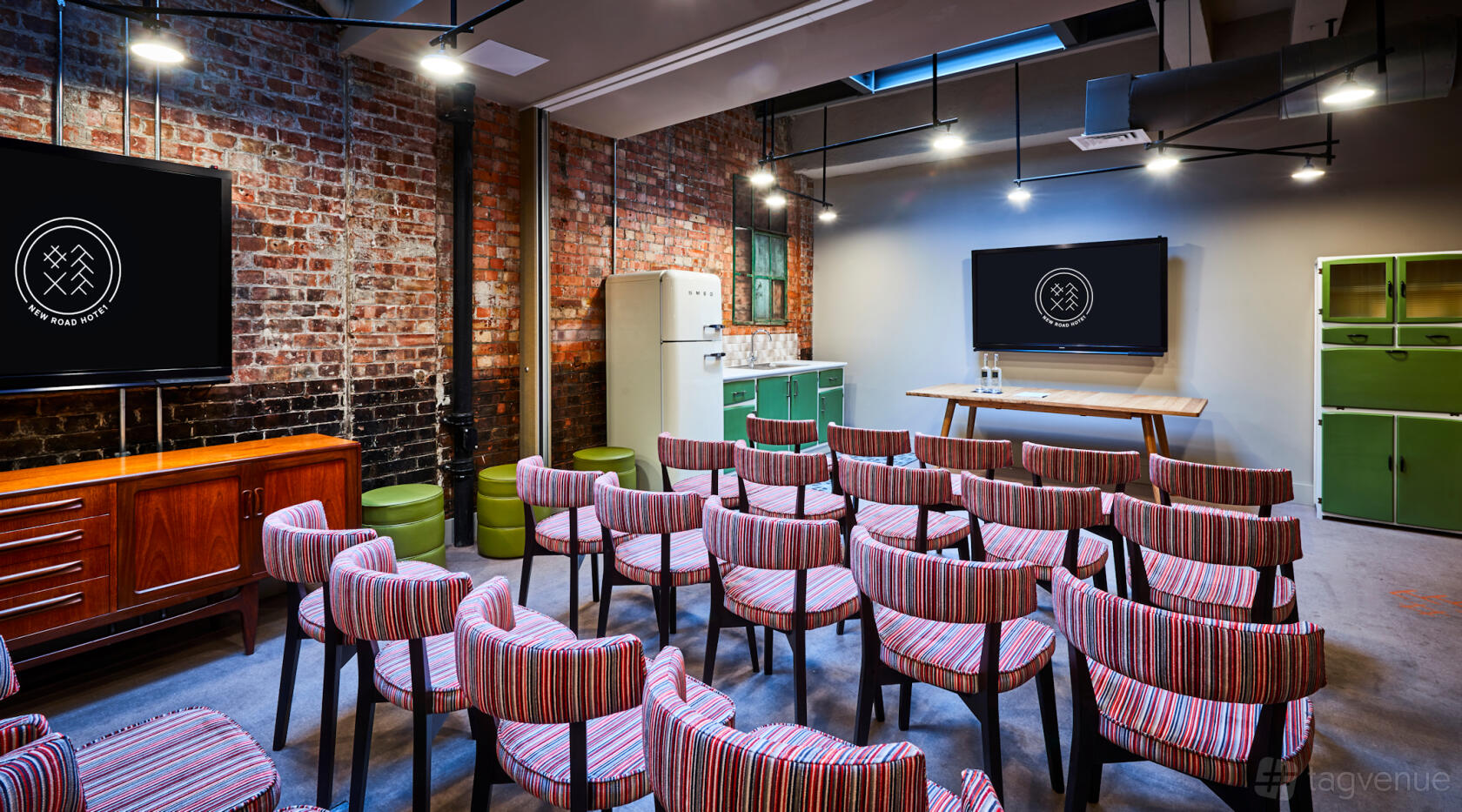 An event space in a hotel with exposed brick walls, striped upholstered chairs, and a presentation screen at New Road Hotel.