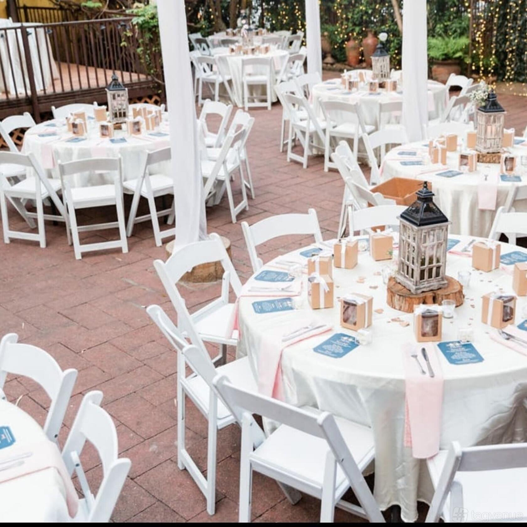 A bar terrace with round tables, white linens, folding chairs, and lantern centerpieces at AvantGarden.