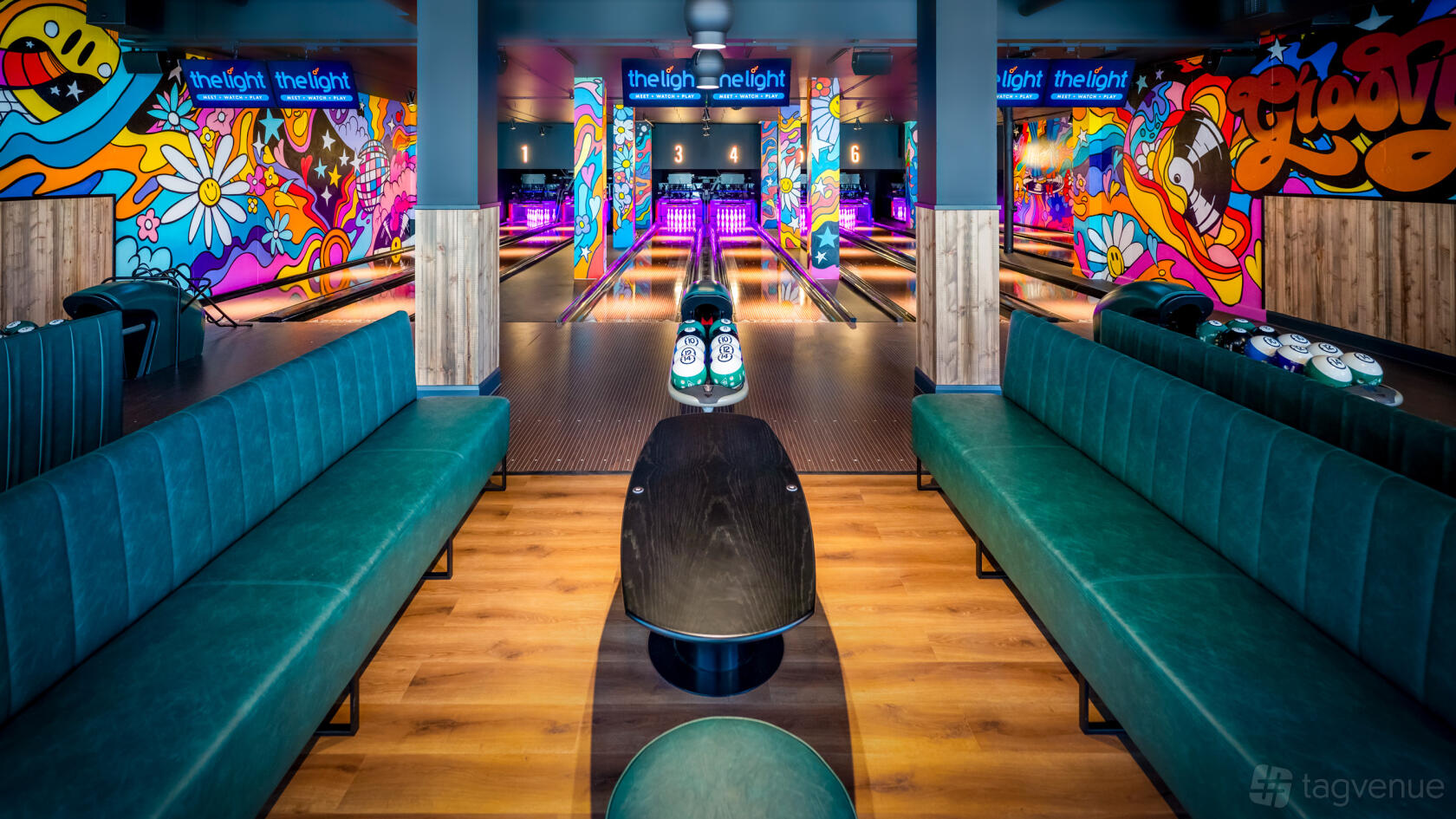 A bowling alley with colorful graffiti murals, illuminated lanes, and green velvet seating at The Light Redhill.