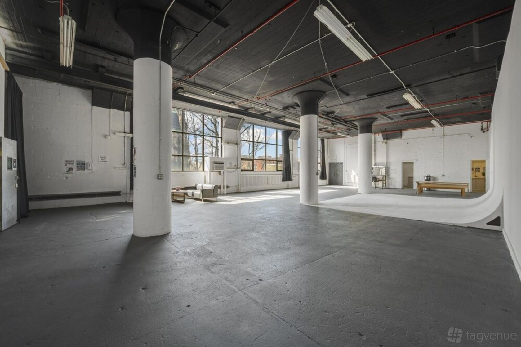 A photo studio with large industrial windows, seamless white cyclorama wall, and concrete floors at HOOK Studios.