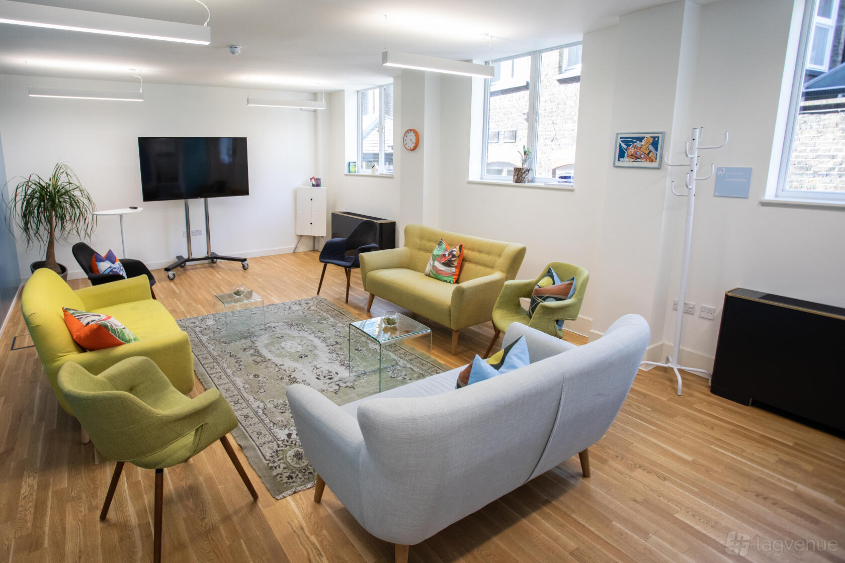 An event space with colorful sofas, a rug, large windows, and a wall-mounted TV at Wallacespace Spitalfields.