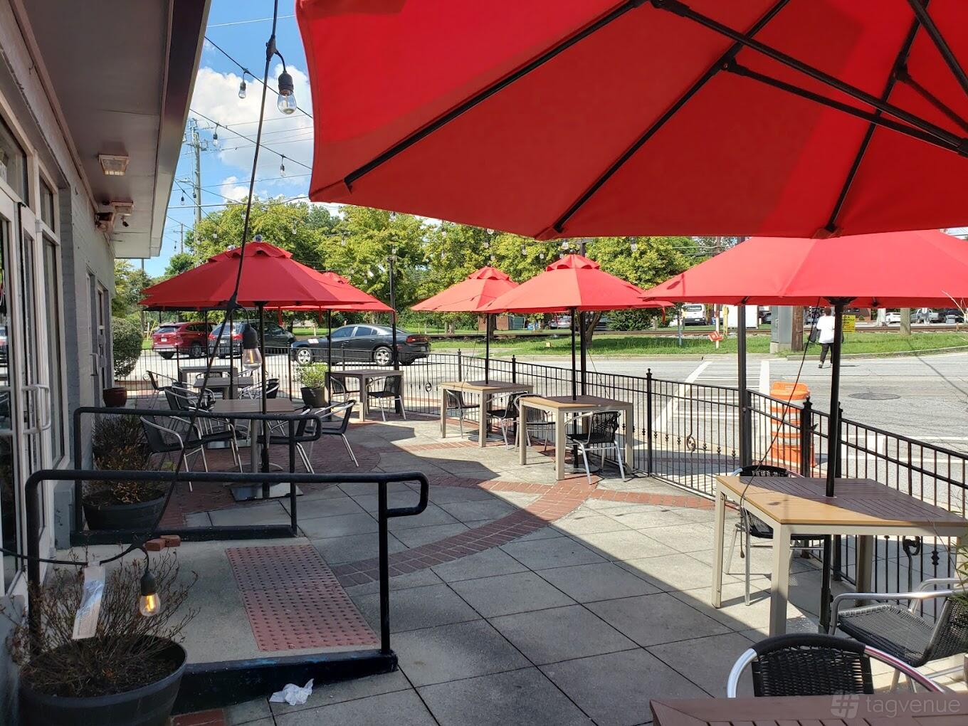An outdoor patio with red umbrellas, black metal chairs, and small tables at Dua Hapeville.