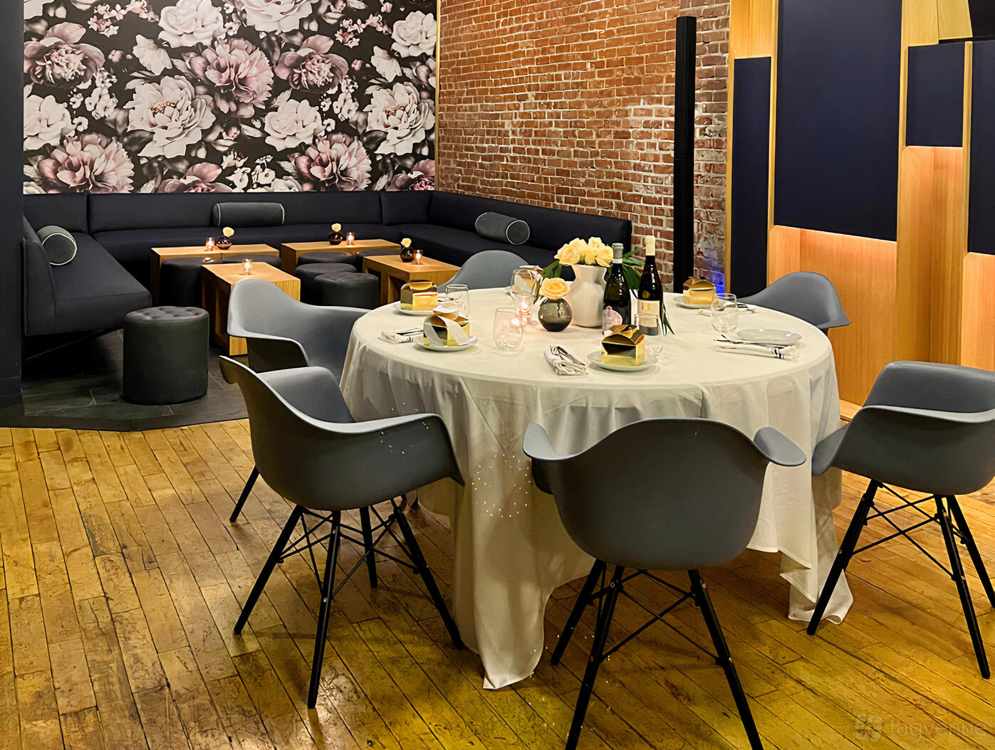 An event space in a restaurant with exposed brick walls, floral accent wallpaper, and a round table with gray chairs at Union Restaurant.
