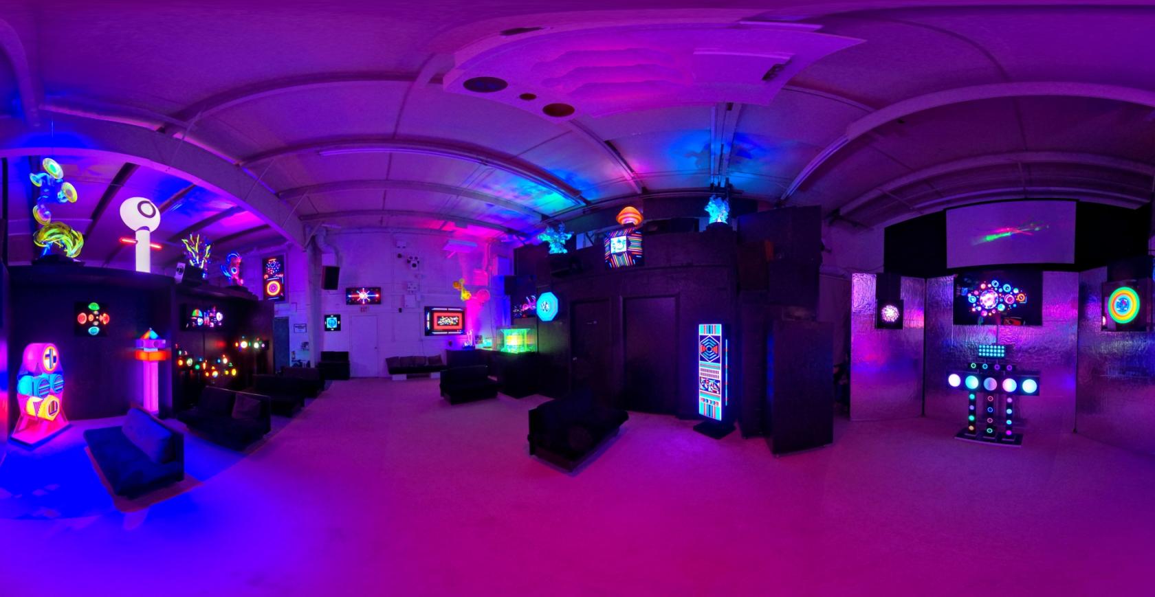 A gallery with neon light installations, glowing panels, and illuminated sculptures at Lumonics Light & Sound Gallery.