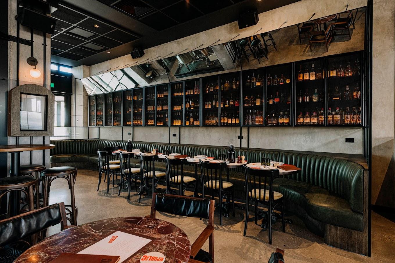 An event space with dark green tufted banquette seating, marble tables, and a wall of glass-front liquor shelves at Republic Tavern Brew-Pub.