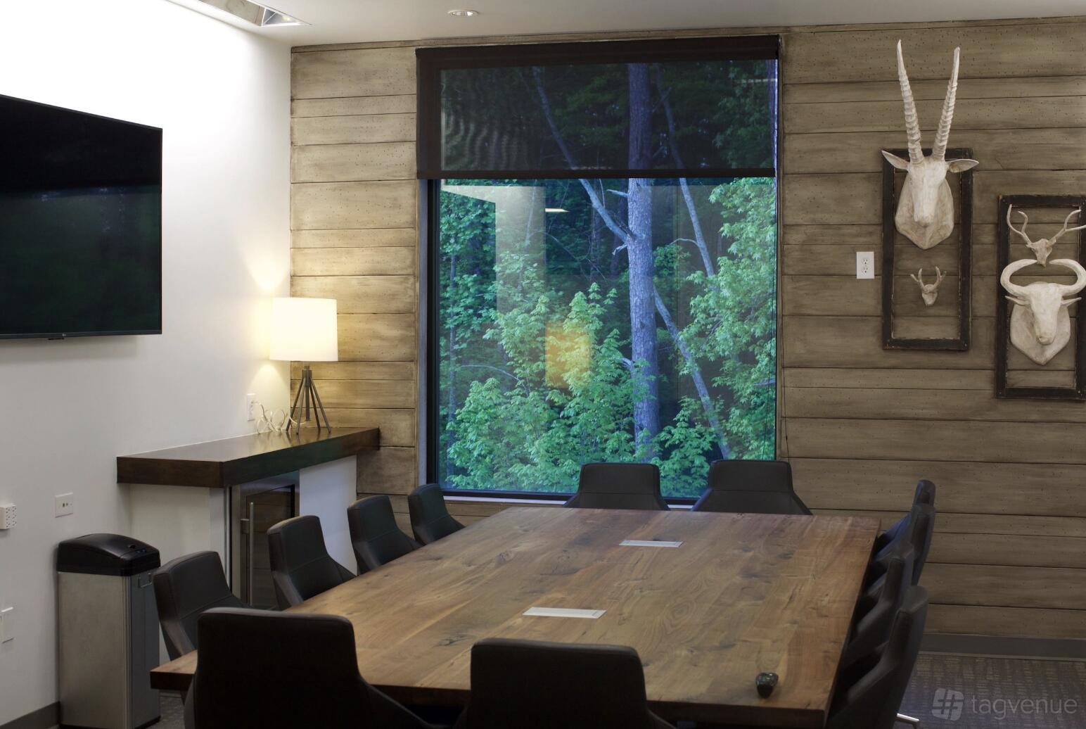 An event space with a large wooden table, black chairs, animal wall art, and a window overlooking trees at ROAM ALPHARETTA.
