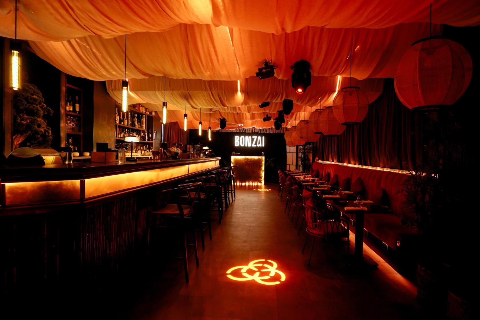 An event space in a restaurant with draped fabric ceiling, warm lighting, and a central bar at Bonzai London.