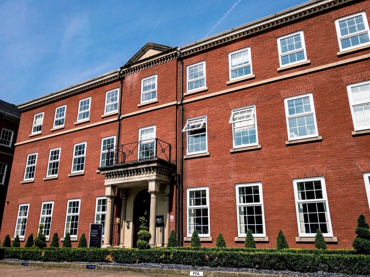 A red brick meeting centre with white-trimmed windows, decorative entrance columns, and manicured hedges at Bartle House.