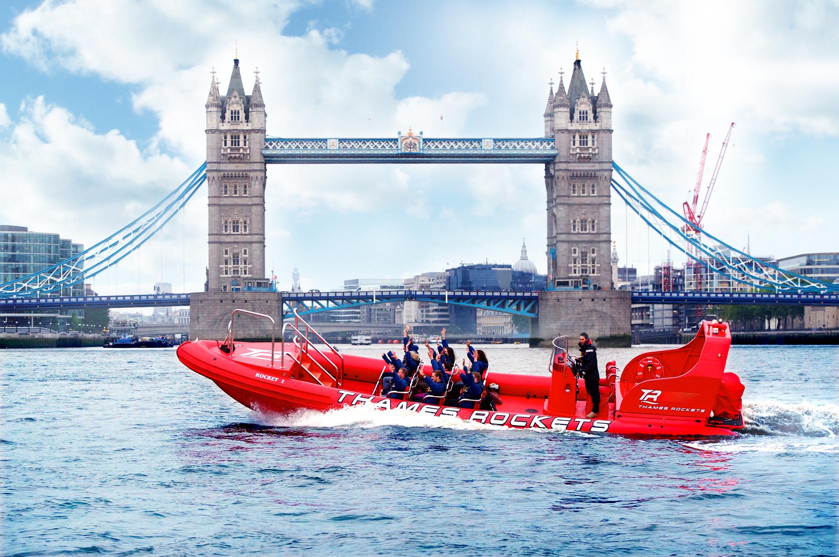 A sightseeing boat with open seating and red hull cruising past Tower Bridge at Thames Rockets.