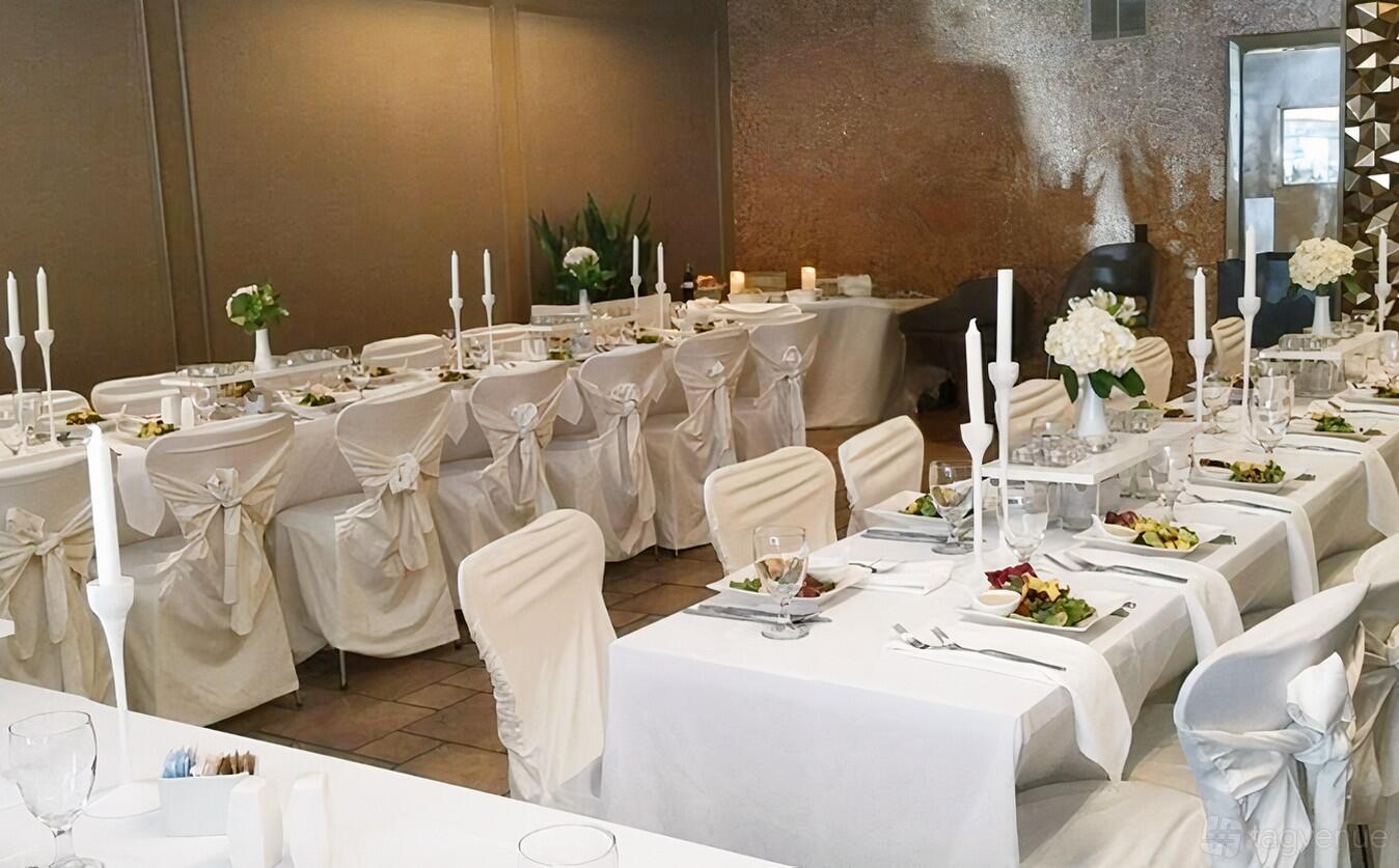 A restaurant with rows of banquet tables draped in white linens and chairs with white sashes at Milk ‘N Honey.