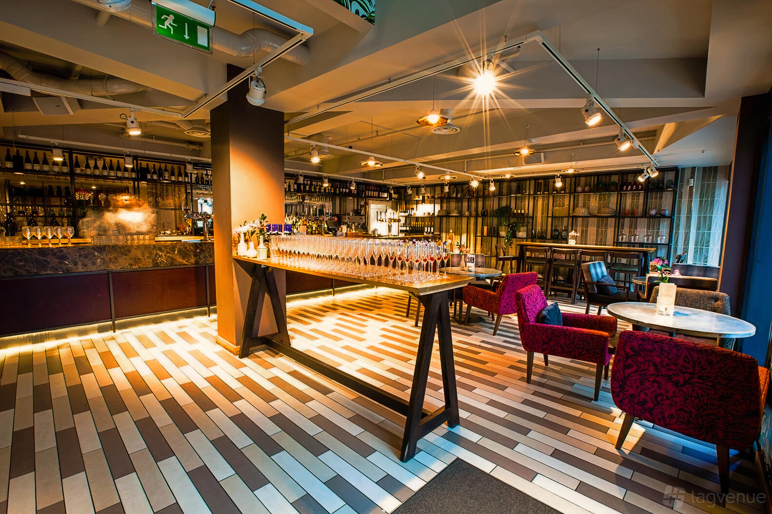 An event space with a long table set with glasses, patterned flooring, and a bar backdrop at The Fable.