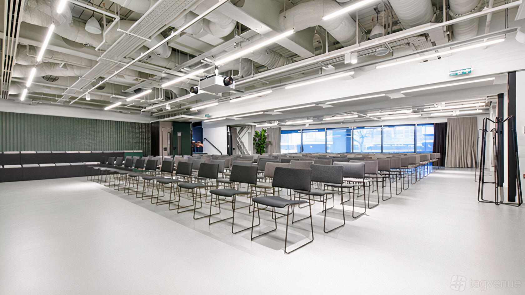 An auditorium with rows of gray chairs, floor-to-ceiling windows, and exposed ceilings at Storey Club Paddington.