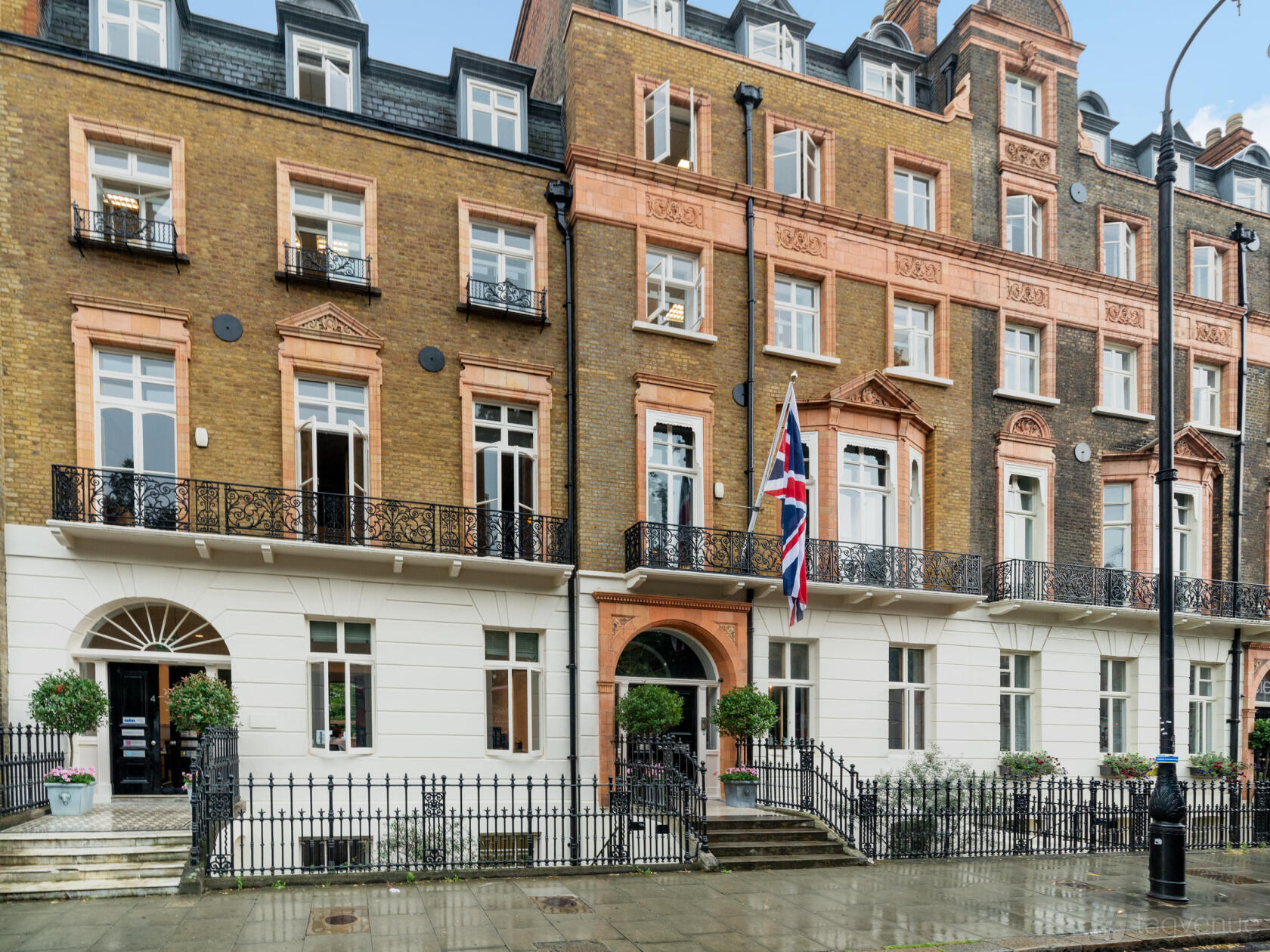 A historic building with ornate brickwork, arched windows, black iron railings, and a UK flag at Russell Square.