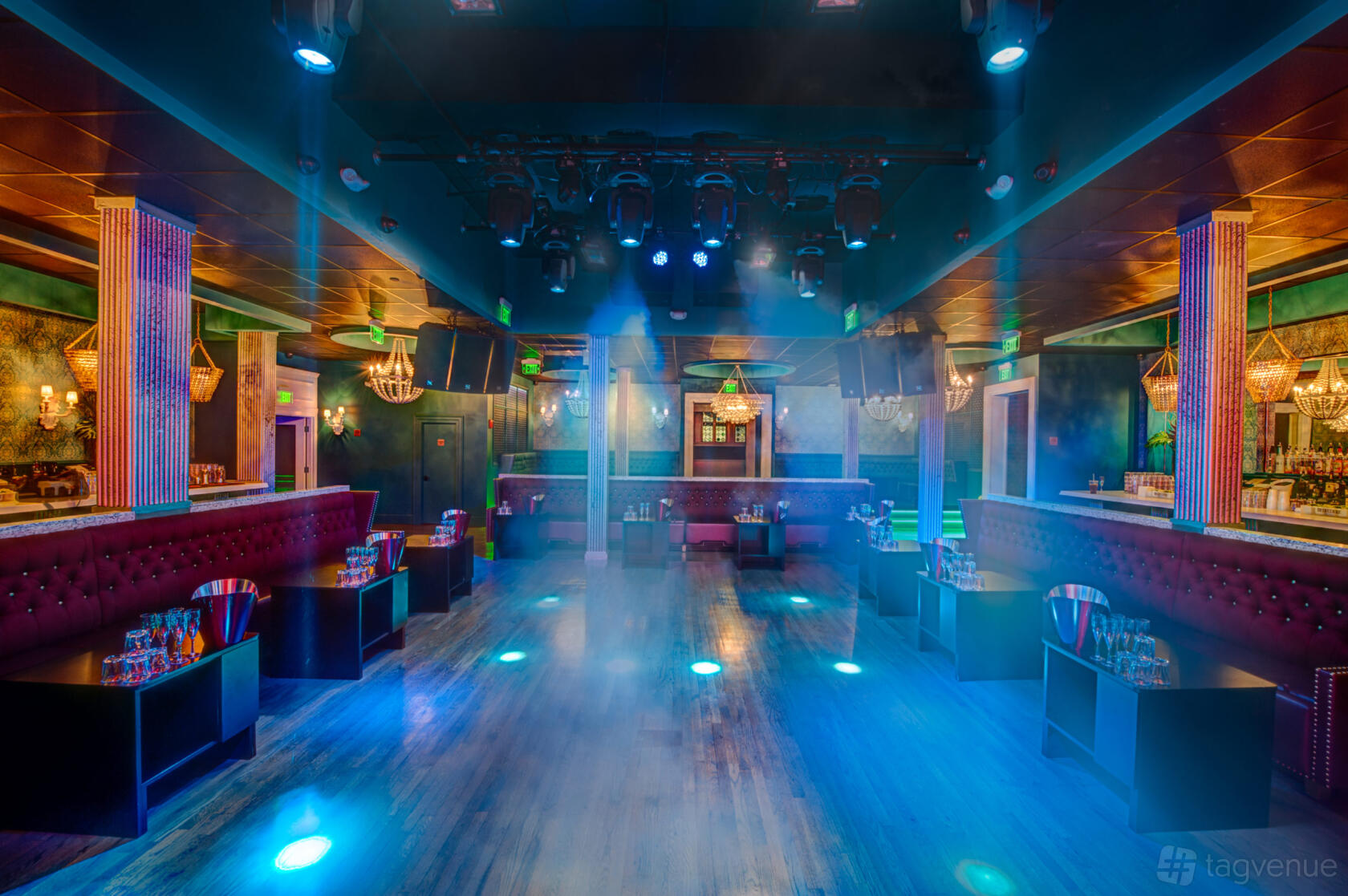 A nightclub with colorful lighting, dance floor, plush banquette seating, and decorative chandeliers at ICON.