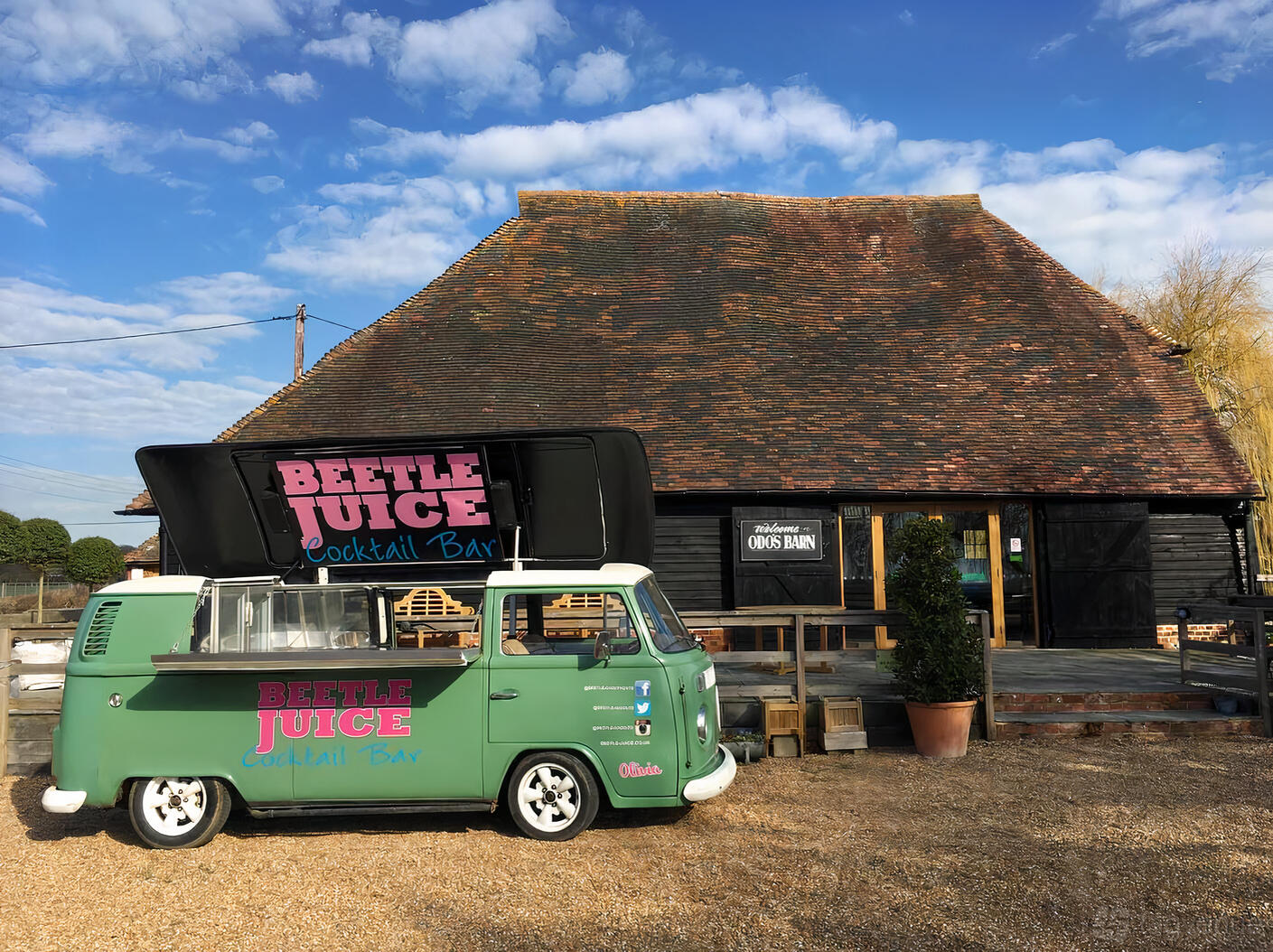 A rustic barn with a weathered timber exterior, pitched roof, and a vintage cocktail van at Odo's Barn.