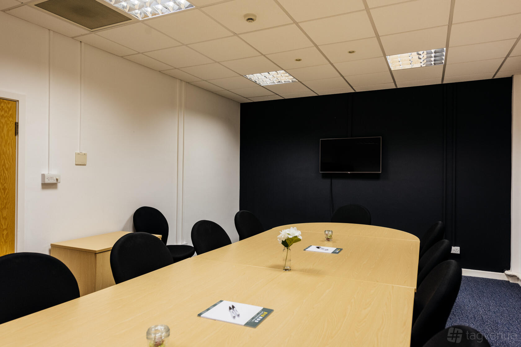 A meeting room with a long oval table, black chairs, wall-mounted TV, and minimal decor at Melton Court.