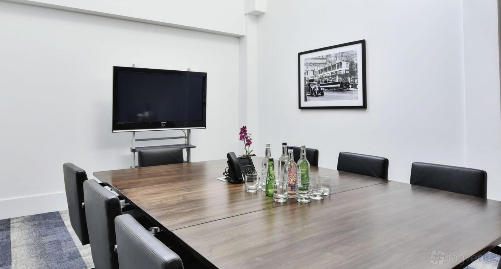 A meeting room with a wooden conference table, black chairs, wall-mounted TV, and bottled water at 29 Farm Street.