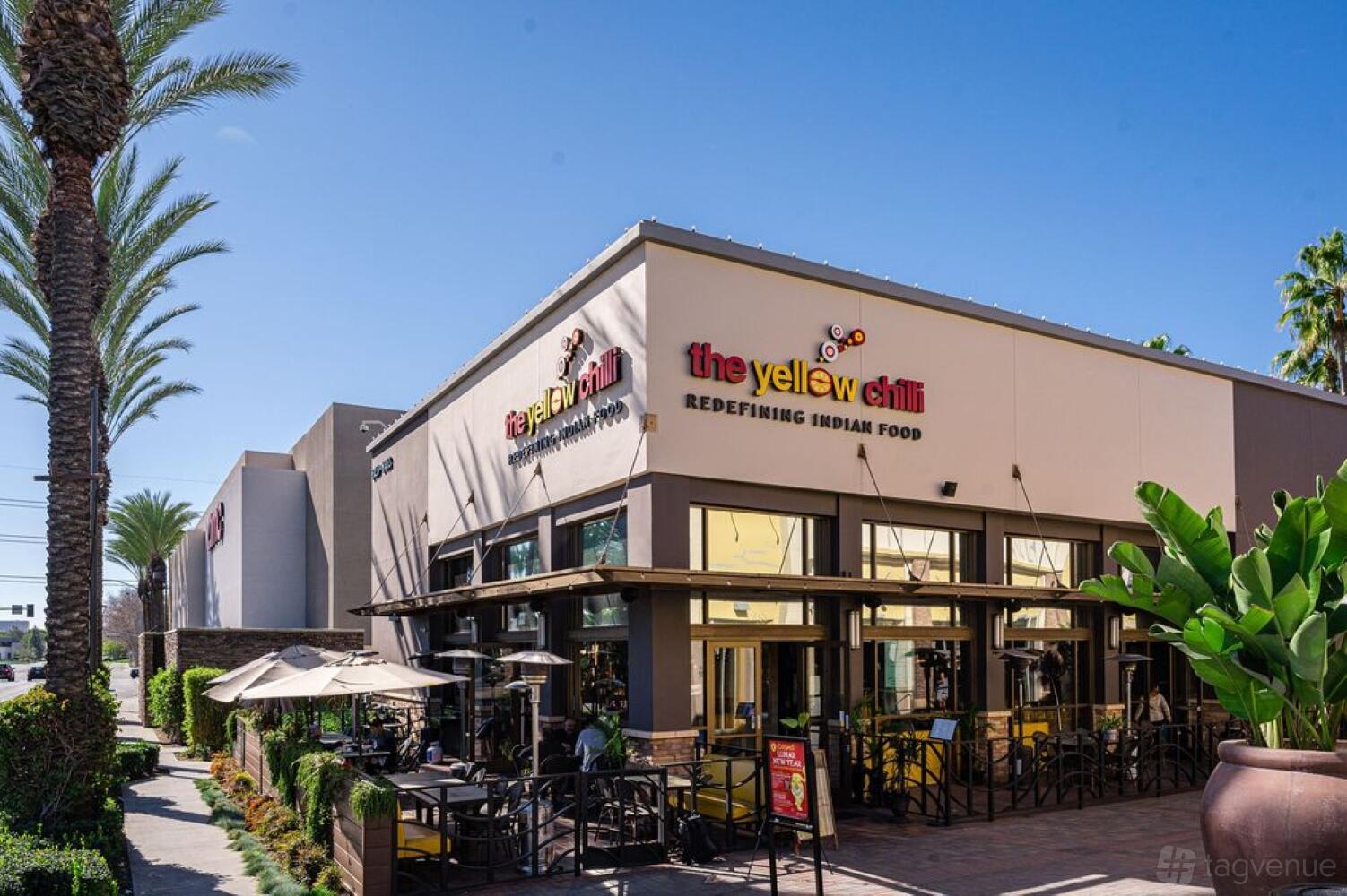 A restaurant with outdoor patio seating, large windows, and yellow umbrellas at The Yellow Chilli Tustin.