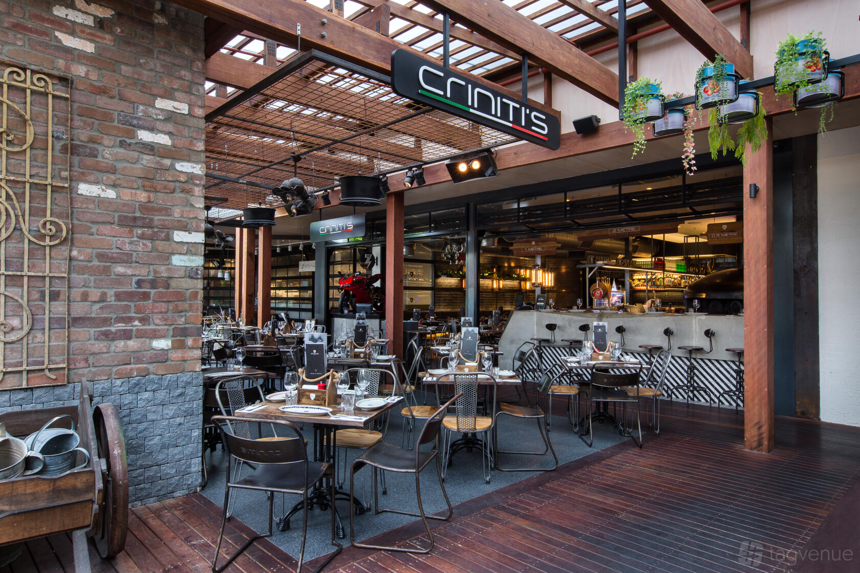 An outdoor dining area with wooden pergola, hanging plants, and black metal tables at Criniti's Kotara.