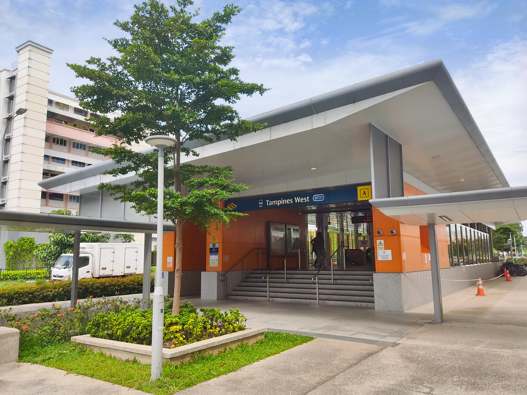 An exterior view of Tampines West MRT station with a covered entrance and surrounding greenery at Tampines West MRT Classroom Space.