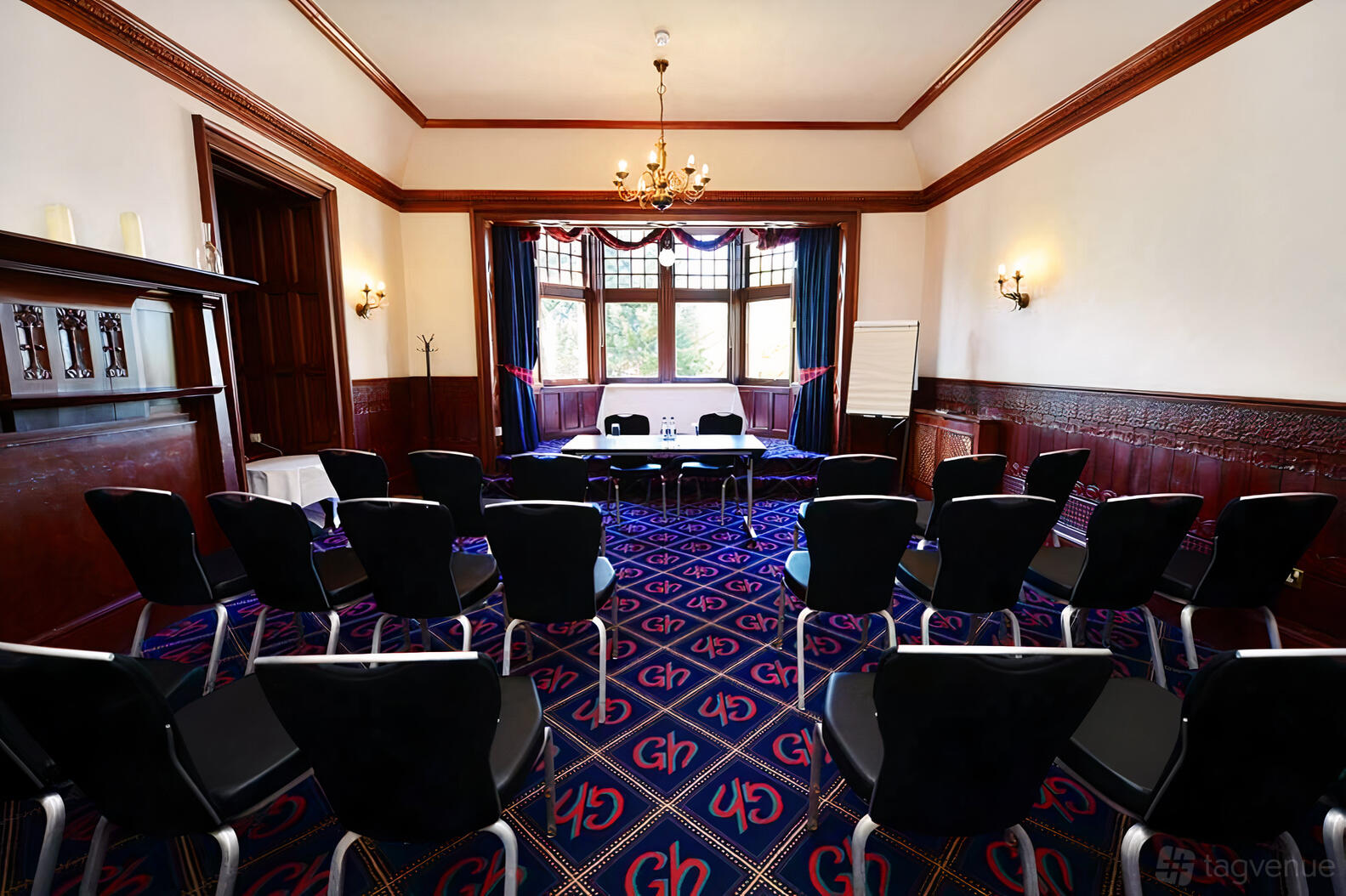 A hotel meeting room with patterned carpet, chandelier lighting, and rows of black chairs at The Glynhill Hotel.