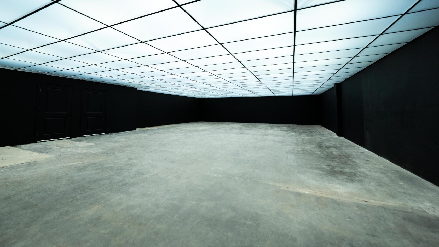 A photo studio with a grid-patterned illuminated ceiling, black walls, and a concrete floor at Yukon Studios.