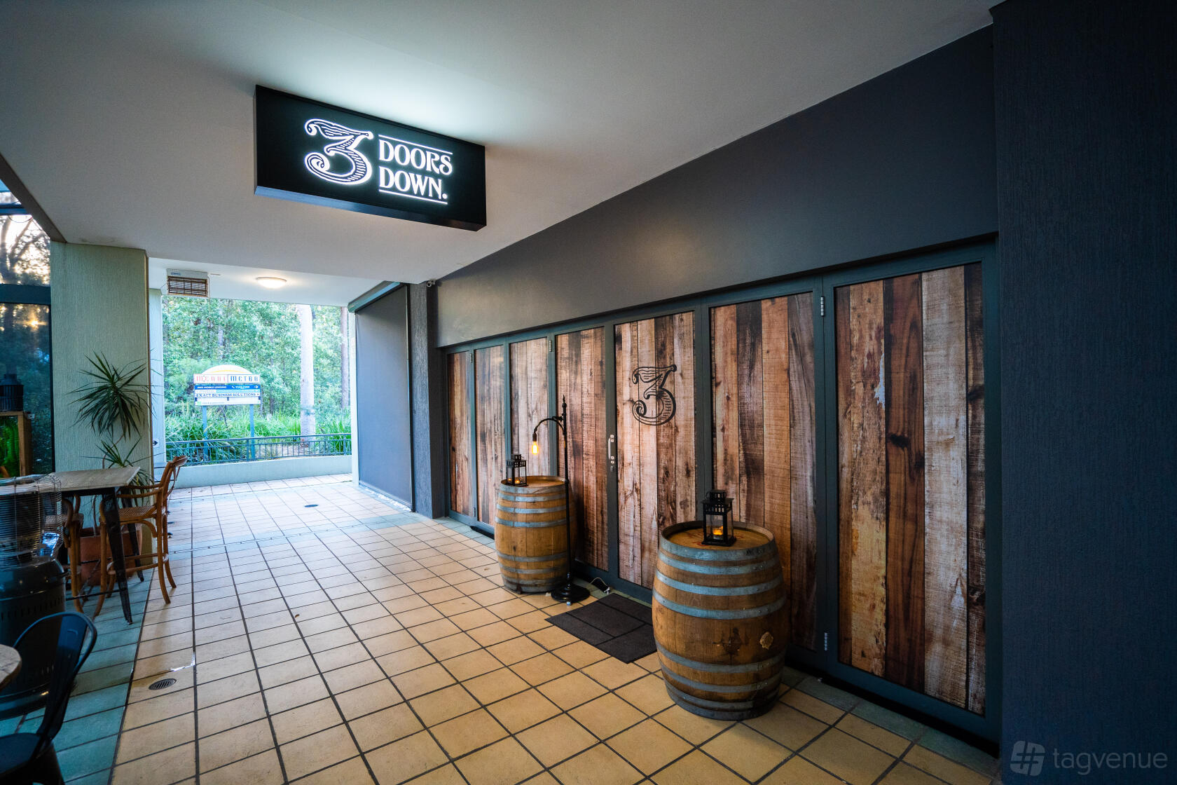 A restaurant entrance with wooden barrel decor, rustic wood paneling, and lantern lighting at 3 Doors Down.