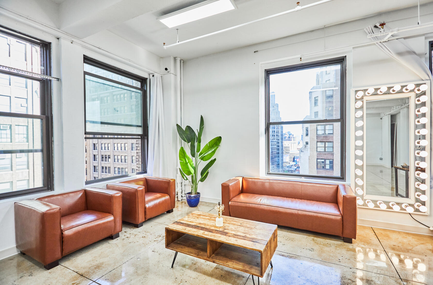 A photo studio with large windows, city views, brown leather chairs, and a lighted vanity mirror at Manhattan Skyline event space.