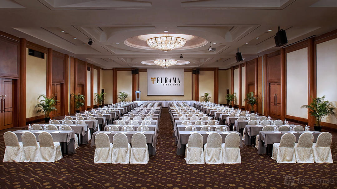 A hotel ballroom with chandeliers, banquet seating at round tables, and a stage at Furama RiverFront.