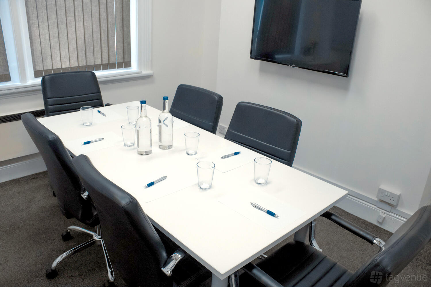 A meeting room with a rectangular table, black chairs, a wall-mounted TV, and water bottles at Oxford Circus.