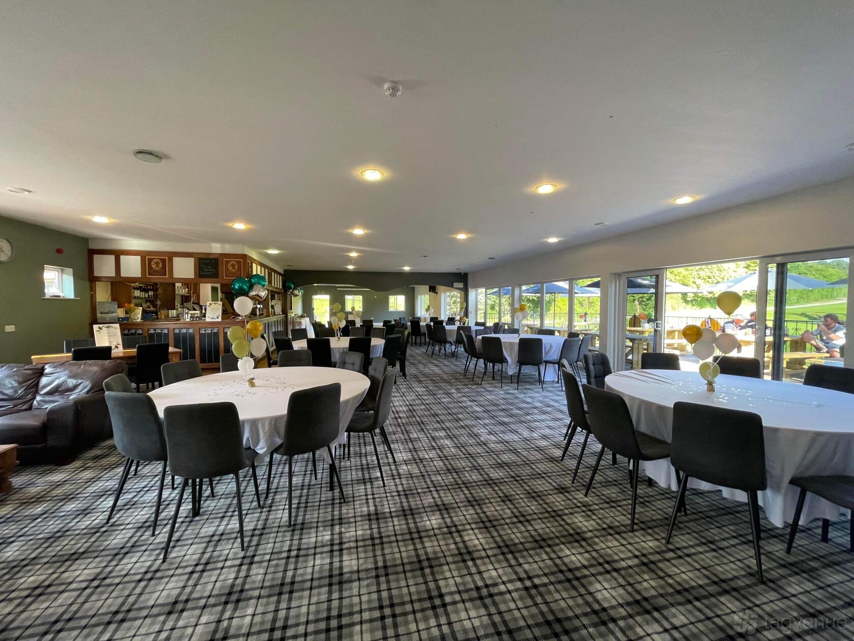 A function room with round tables covered in white linens, grey chairs, and large windows at Leominster Golf Club.