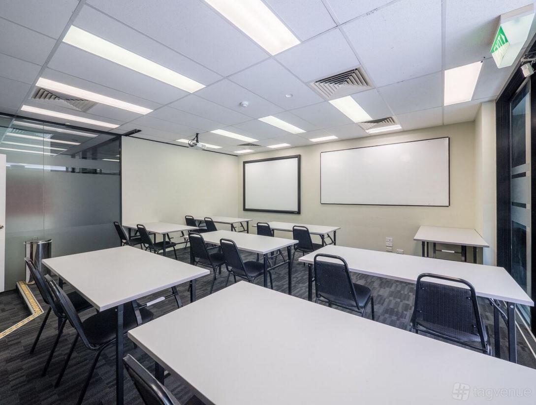 A training room with whiteboards, rows of rectangular tables, and black chairs at M1 Business Centre.