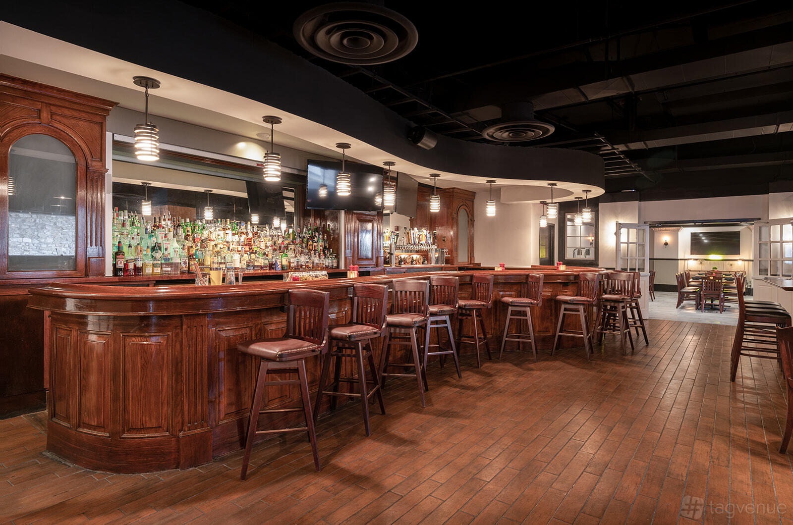A restaurant bar area with a long polished wood bar, bar stools, and pendant lighting at Potomac Social Tavern.