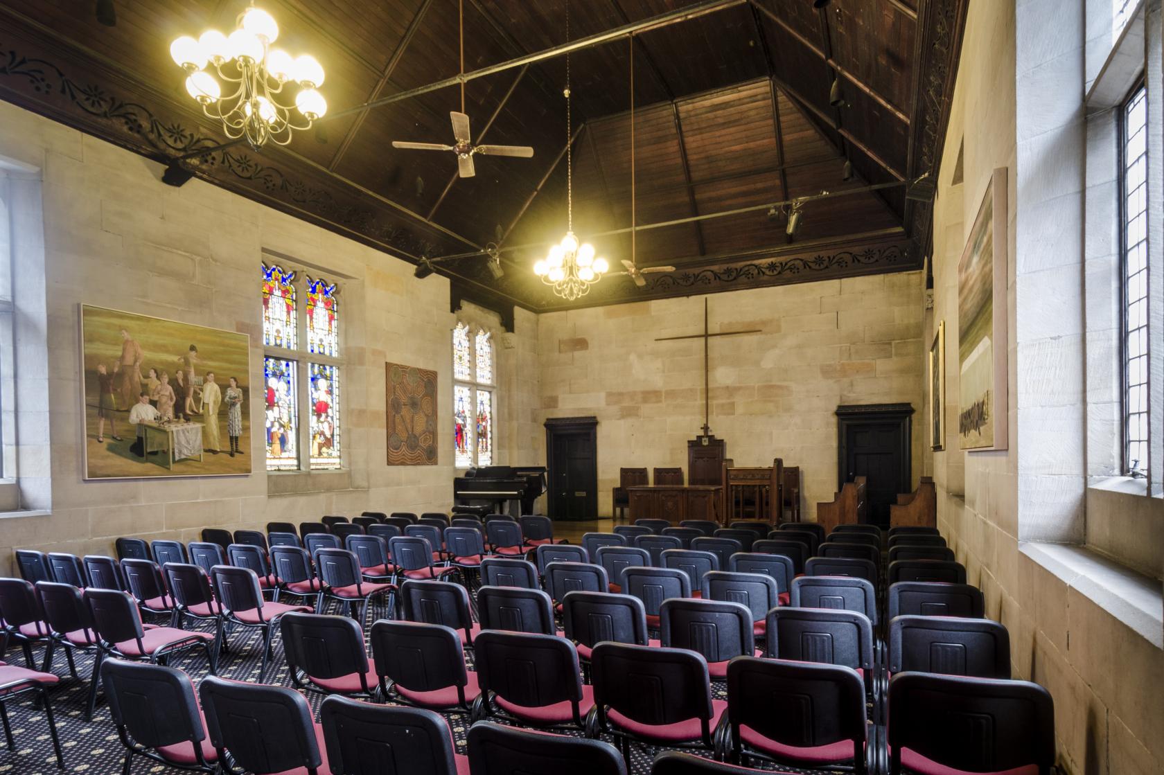 A chapel with stained glass windows, wooden ceiling beams, and rows of chairs at St Andrew's College University of Sydney.