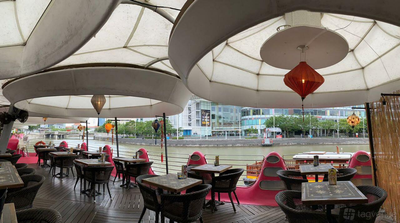 A riverside terrace with round lanterns, retractable canopy, and rattan tables at Little Saigon.