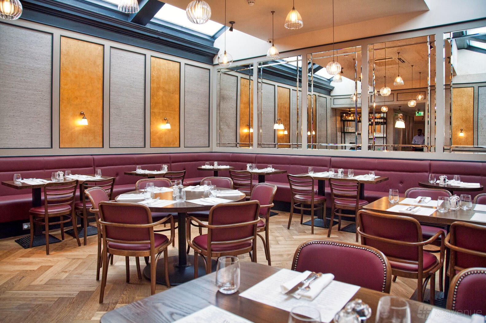 A restaurant with burgundy banquette seating, wooden tables, mirrored walls, and pendant lighting at Côte Brasserie Edinburgh.