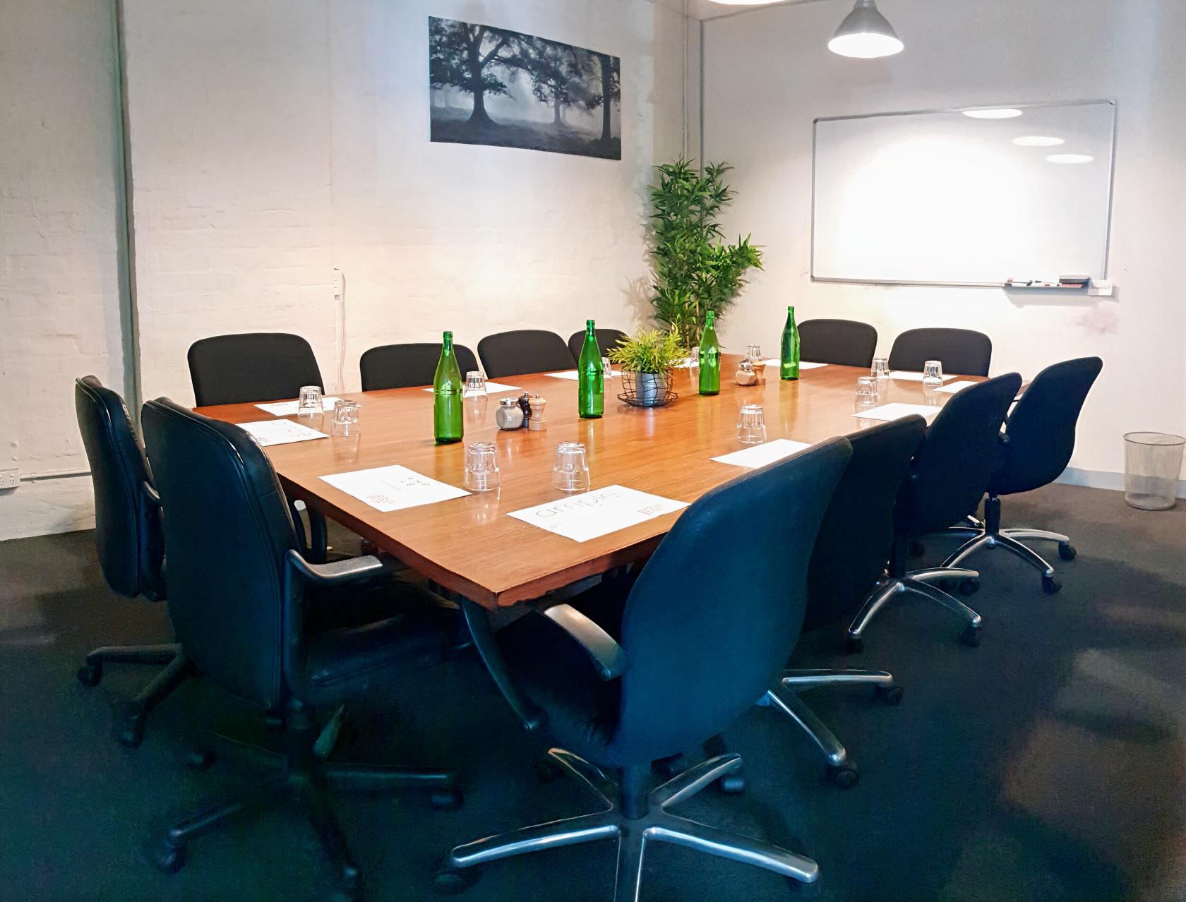 A meeting room with a large wooden conference table, black chairs, green glass bottles, and a whiteboard at Ample Cafe & Bar.