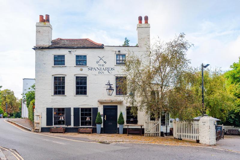 A traditional white-painted pub with black trim, outdoor benches, and tall chimneys at The Spaniards Inn.