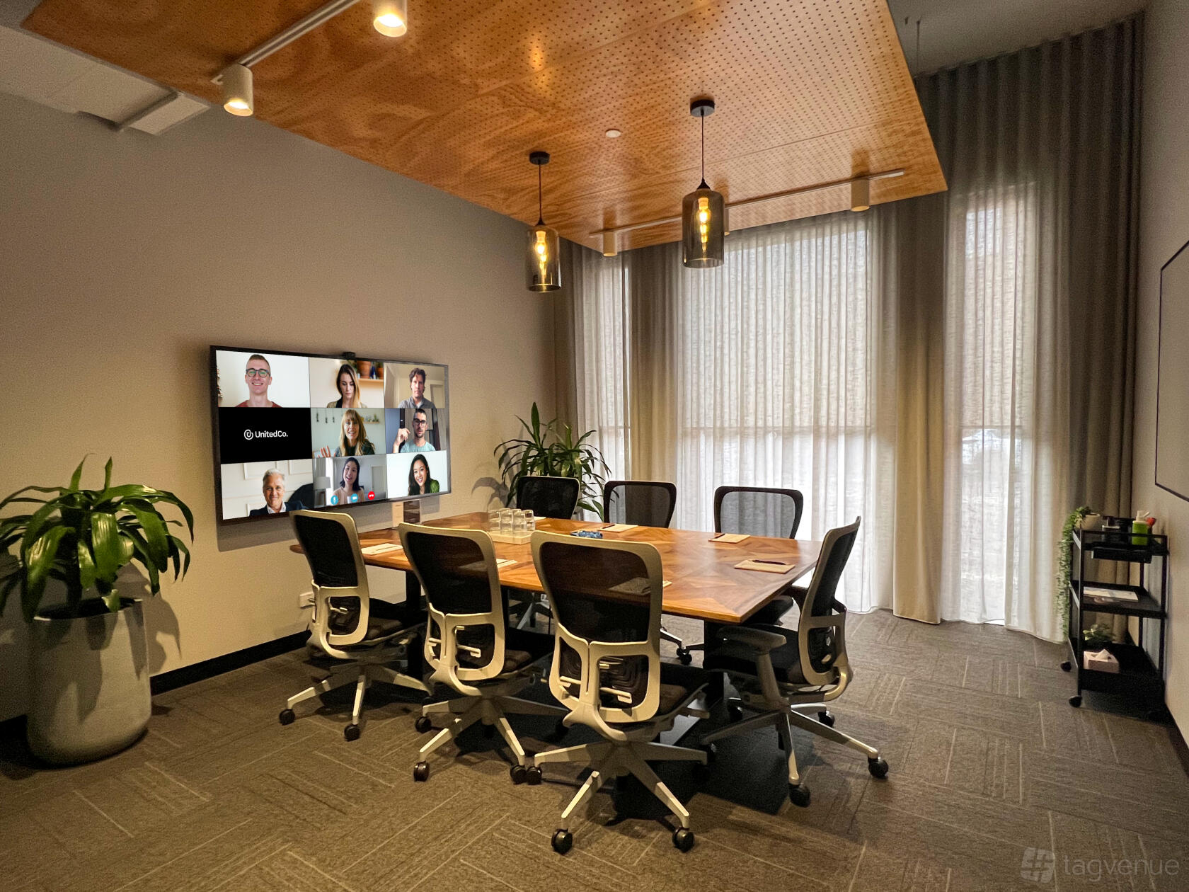 A meeting room with a large wooden table, mesh office chairs, wall-mounted screen, and floor-to-ceiling windows at United Co. Fitzroy.