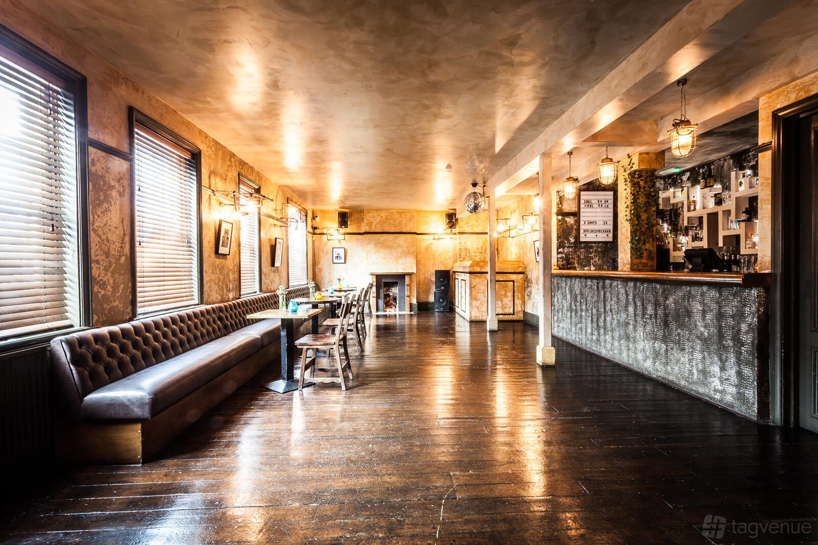 A pub interior with wooden floors, tufted leather banquette seating, and pendant lighting at Prince of Peckham.