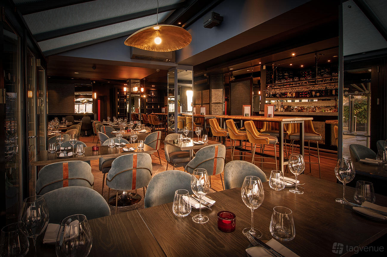 A restaurant with velvet chairs, set tables with wine glasses, and a backlit bar at Gaucho Richmond.