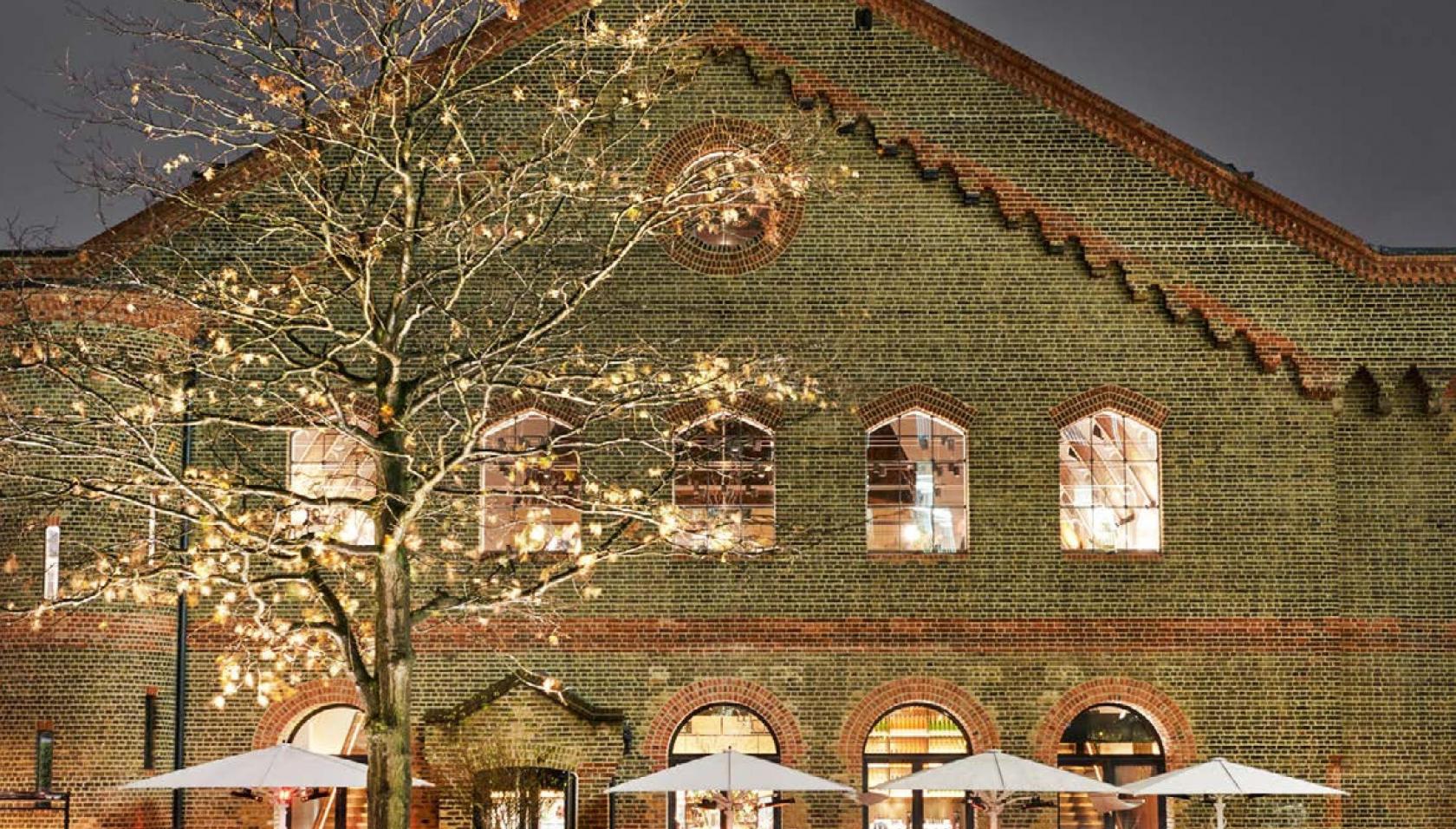 A restaurant with brick facade, arched windows, and outdoor seating with umbrellas at German Gymnasium.